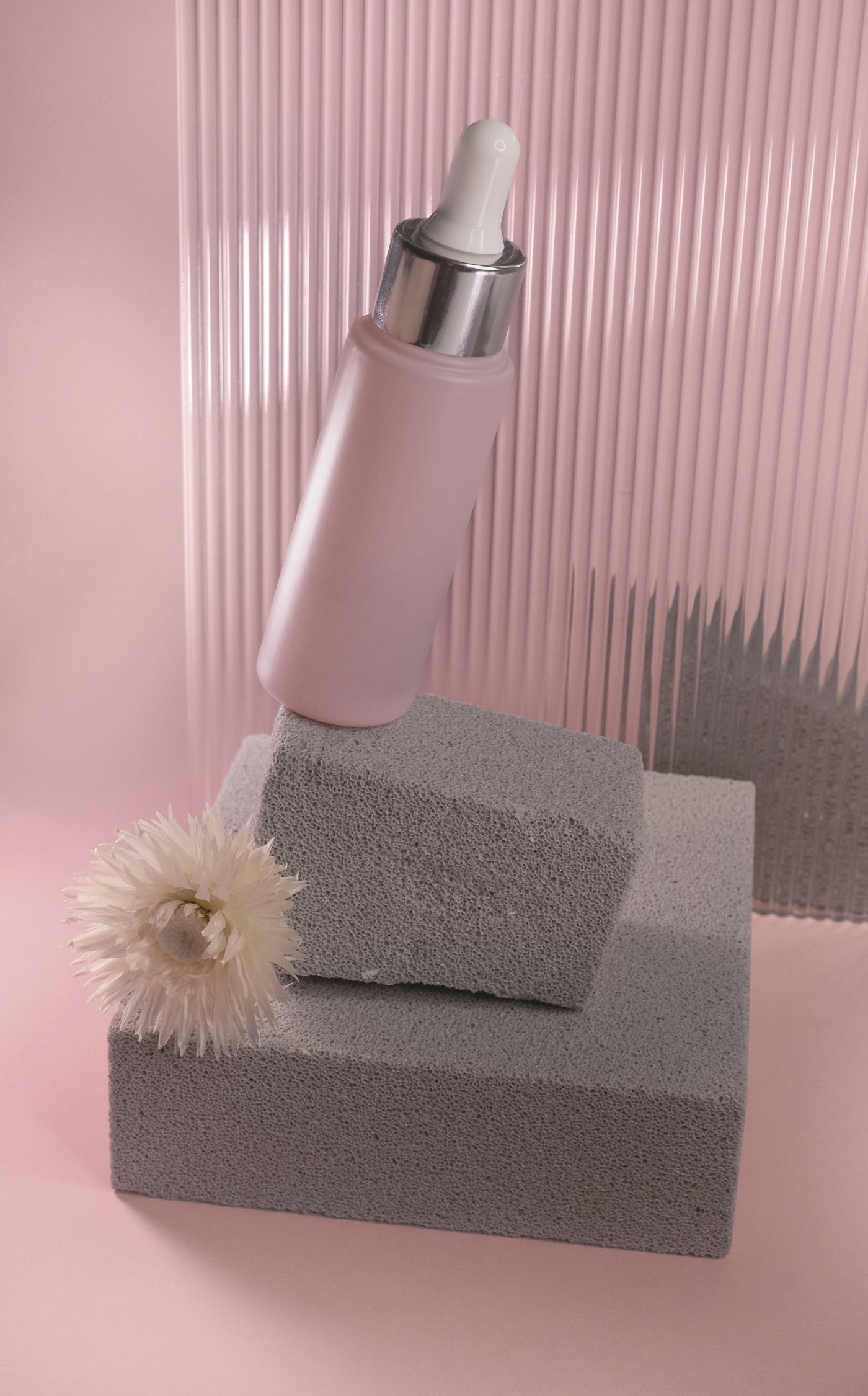 Frasco claro sobre um bloco de concreto, em fundo rosa